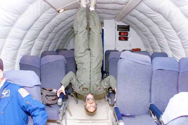 A man hangs upside-down without anything holding him up in the cabin of an aircraft designed to simulate a zero-gravity atmosphere.