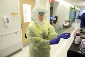 A doctor wearing an apron, head covering and face shield puts on blue gloves as she prepares for a shift treating COVID-19 patients at Johns Hopkins Hospital. 