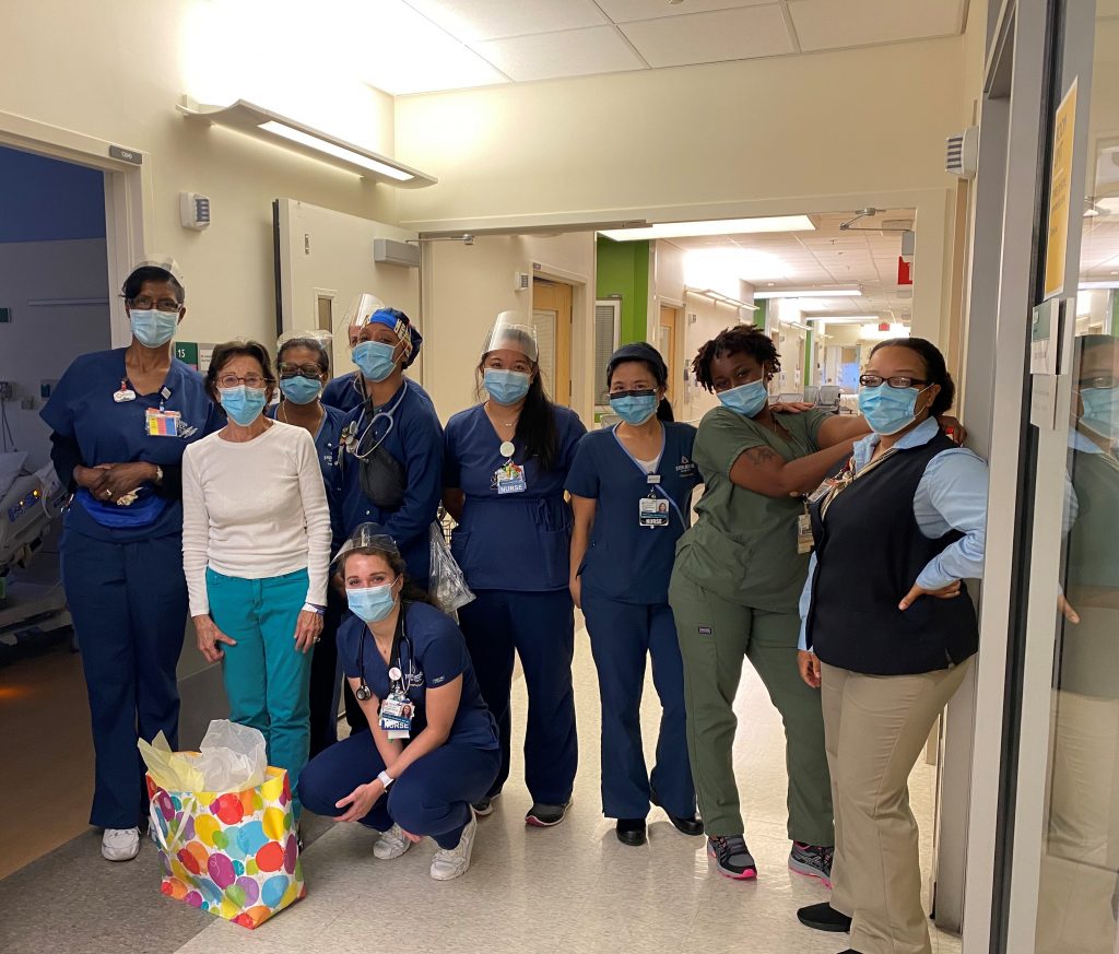 Nine Johns Hopkins Hospital Nursing employees mostly standing and facing outward and wearing dark blue scrubs and face masks.