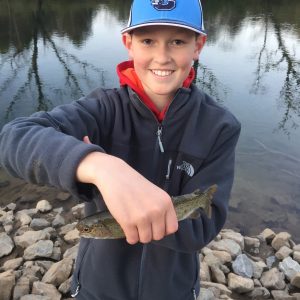 boy in blue jacket and hat smiles holding a fish