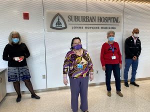 suburban hospital employees wearing masks stand in front of the hospital's sign