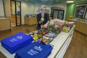 A woman in a mask holds an apple and other fresh produce in the new eat to thrive shop