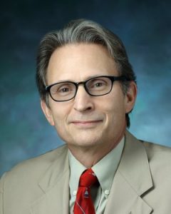 Prostate cancer researcher Bill Isaacs wears glasses, a red, tie, and a khaki blazer