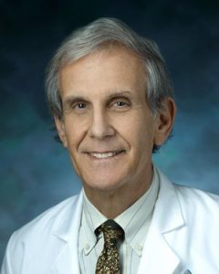 Vestibular neurologist David Zee, who studies eye movement disorders and dizziness, smiles and wears a white medical coat.