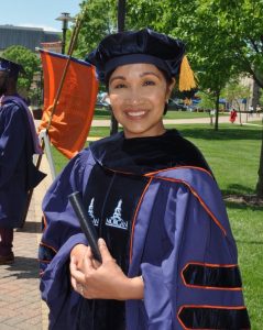 Baltimore County School teacher and HEAT Corps advocate Edralin Pagarigan faces the camera and smiles in a purple and orange graduation cap and gown.