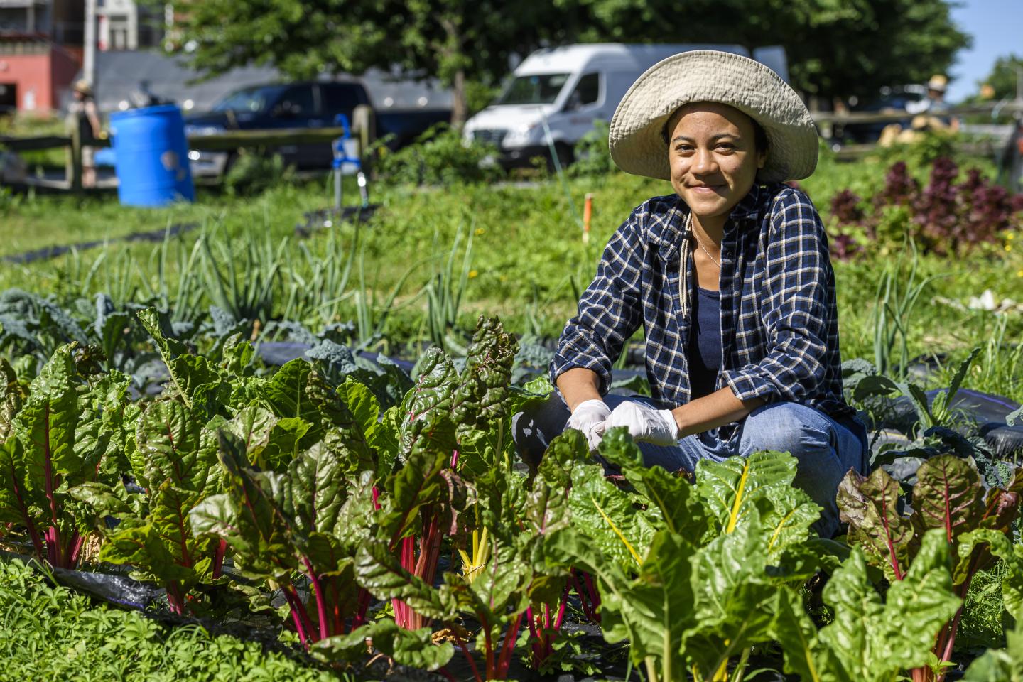 Wearing a hat, Johns Hopkins student Marisa Thomas smiles next to a vegetable gardeb