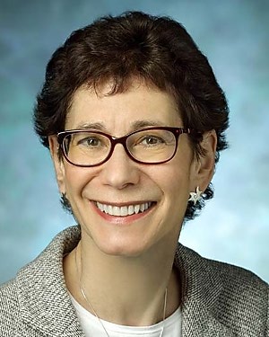 A portrait of Institute of Basic Biomedical Sciences Professor Cynthia Wolberger who has short brown hair, wears glasses and star-shaped earrings, and smiles.