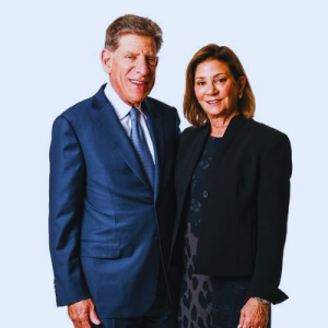 Wilmer Rising Professorship donors Allan and Shelley Holt smile and stand next to one another with Allan in a dark navy suit and Shelley in a black jacket over a dark dress.