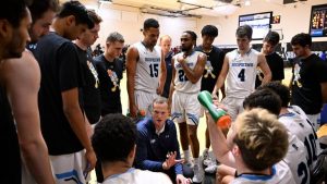 Johns Hopkins basketball coach Josh Loeffler huddles with his players including Sidney Thybulle who is standing.