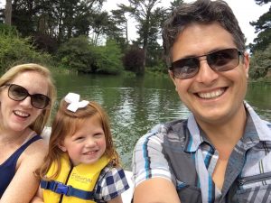 With water and green foliage in the background, Laney Jaymes Foundation founders Brian and Laura Fitzsimons smile and sit on a boat with their daughter Laney Jaymes between them.