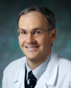 Johns Hopkins cardiologist Dr. Roger Blumenthal smiles and wears a white lab coat, striped shirt, dark blue tie and glasses