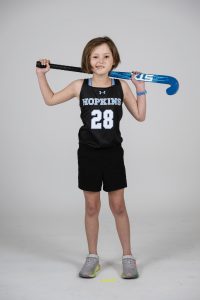 Team IMPACT participant Mackenzie "Kenzie" Opdyke posing with a field hockey stick in a black field hockey uniform