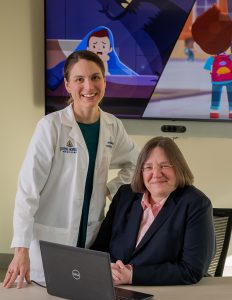 Johns Hopkins psychiatrist Claire Zachik stands in a white lab coat next to Johns Hopkins psychiatrist Karen Swartz who sits behind a computer laptop and wears a pink shirt and dark suit jacket