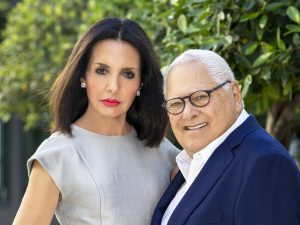 Elizabeth Star has dark shoulder-length hair and wears a silver top as she stands next to her husband Stanley Star who smiles, has white cropped hair, smiles and wears glasses, a white shirt and navy jacket