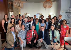 More than 20 alumni from the Class of 1994 are pictured together at their 30th class reunion. They are huddled together inside a banquet hall smiling.