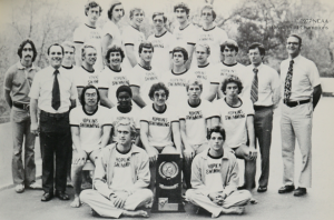 The 1977 Johns Hopkins men's swimming team and coaches are all smiling and posed around their NCAA championship trophy.