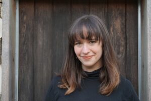 Michelle Fitzgerald is smiling into the camera. She's wearing a black sweater and standing in front of a wooden backdrop.