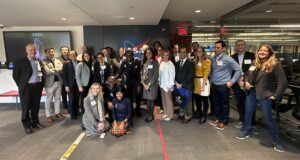 The Leadership Fellows are gathered in a group smiling in front of the NASA sign in the Space Telescope Science Institute Command Center.