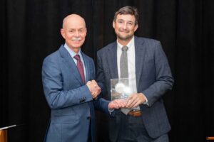 Johns Hopkins University School of Medicine Dean Theodore DeWeese stands to the left of Dr. Matthew Ladra and presents him with a square-shaped plaque and shakes his hand