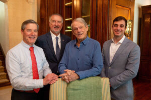 Standing together between an arm chair and tall paneled wood shelf are Wilmer physician Neil Bressler, Wilmer director Peter McDonnell, donor James Gills and Wilmer physician Michael Sulewski