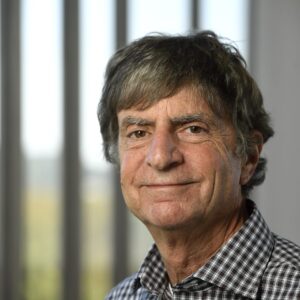 Steven Ross is standing in front of a window and smiling.