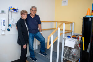 Laura and Tony Roussos are standing and smiling on the custom-built steps their gift supported. The three steps are gray with wood-colored railings. 